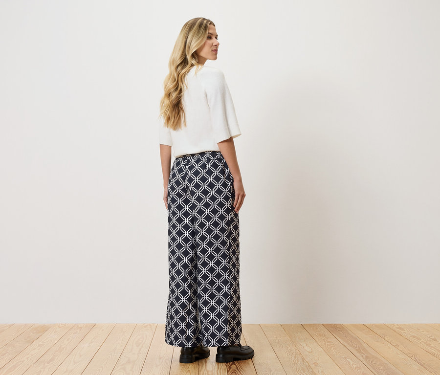Frau trägt ein weißes Oberteil und eine lange, marineblaue Hose mit weißem geometrischem Muster.