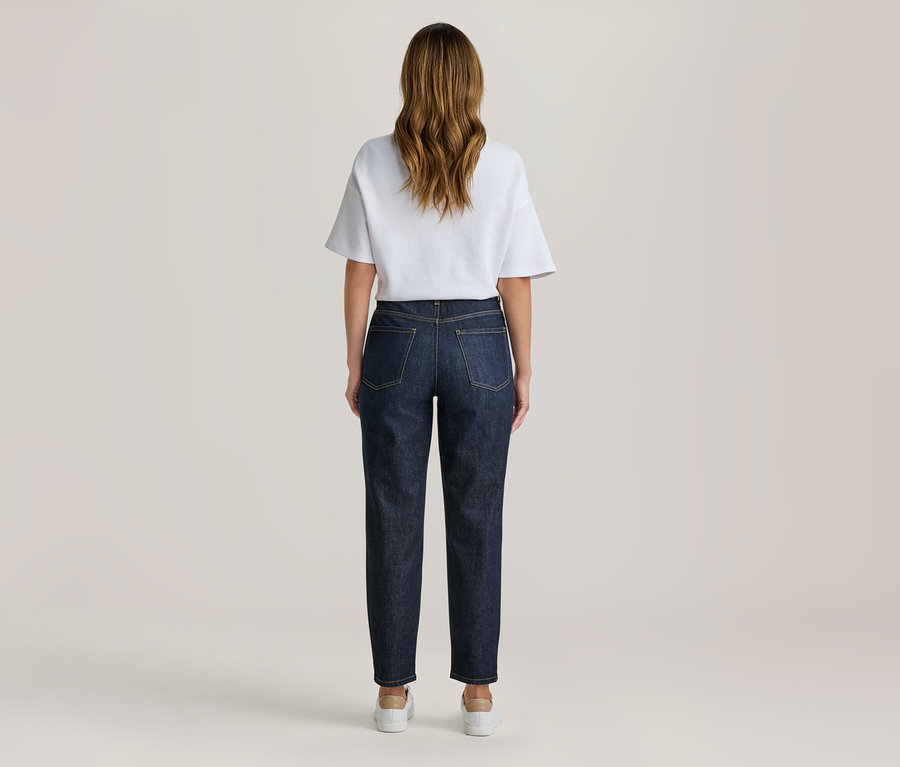 Frau von hinten stehend, trägt ein weißes T-Shirt und dunkelblaue Jeans mit hellen Sneakers.