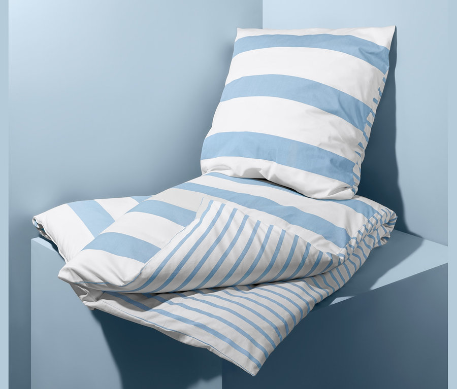 Auf hellblauem Hintergrund liegt ein Bettwäsche-Set mit blauen und weißen Streifen.
