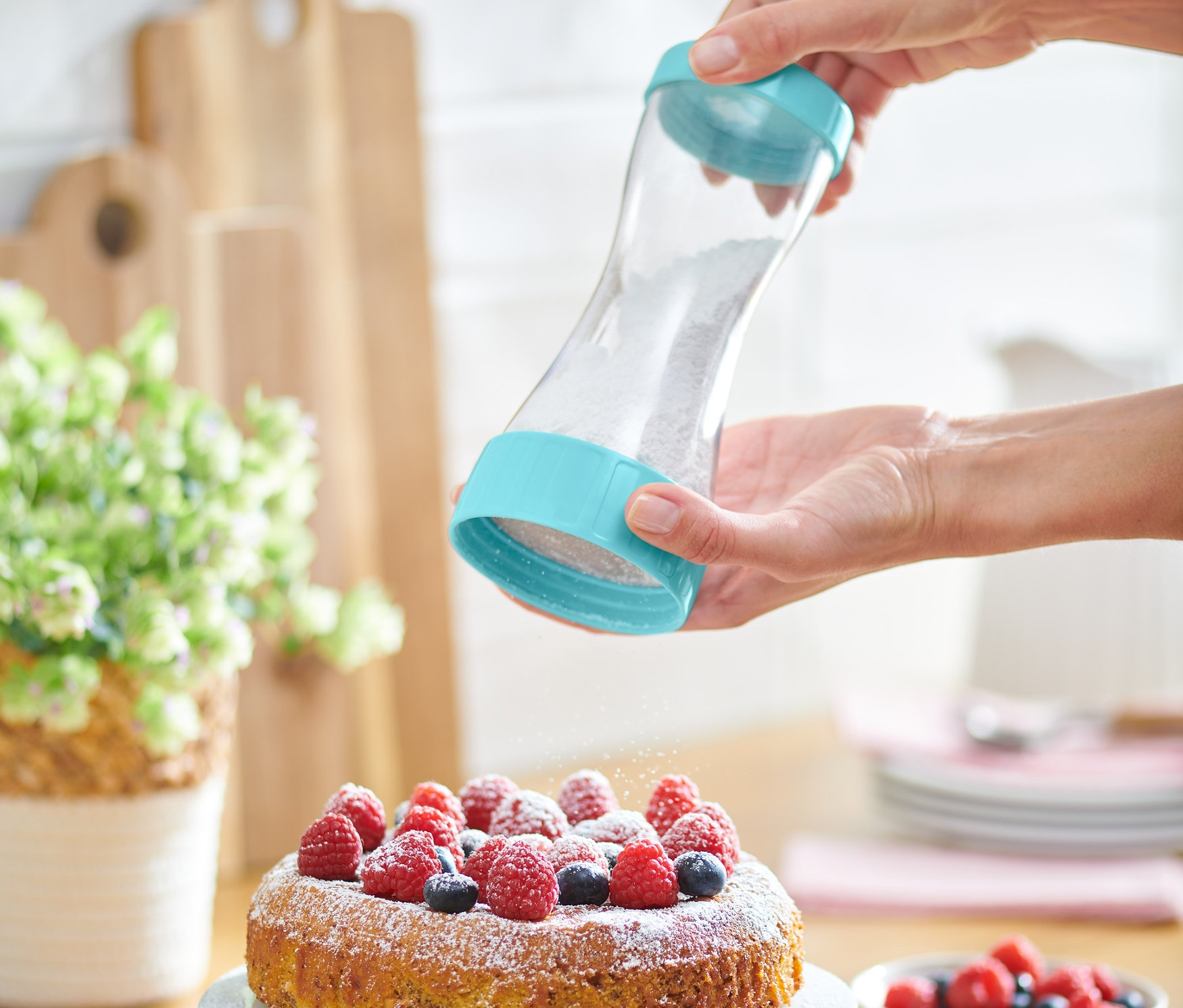Frau bestreut einen Kuchen mit Puderzucker mit einem Puderzuckerstreuer.
