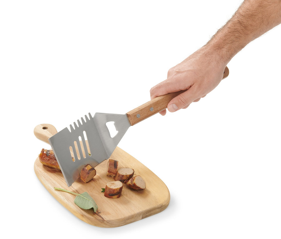 Eine Hand hält ein BBQ-Multitool über ein Holzbrett mit geschnittener Wurst.