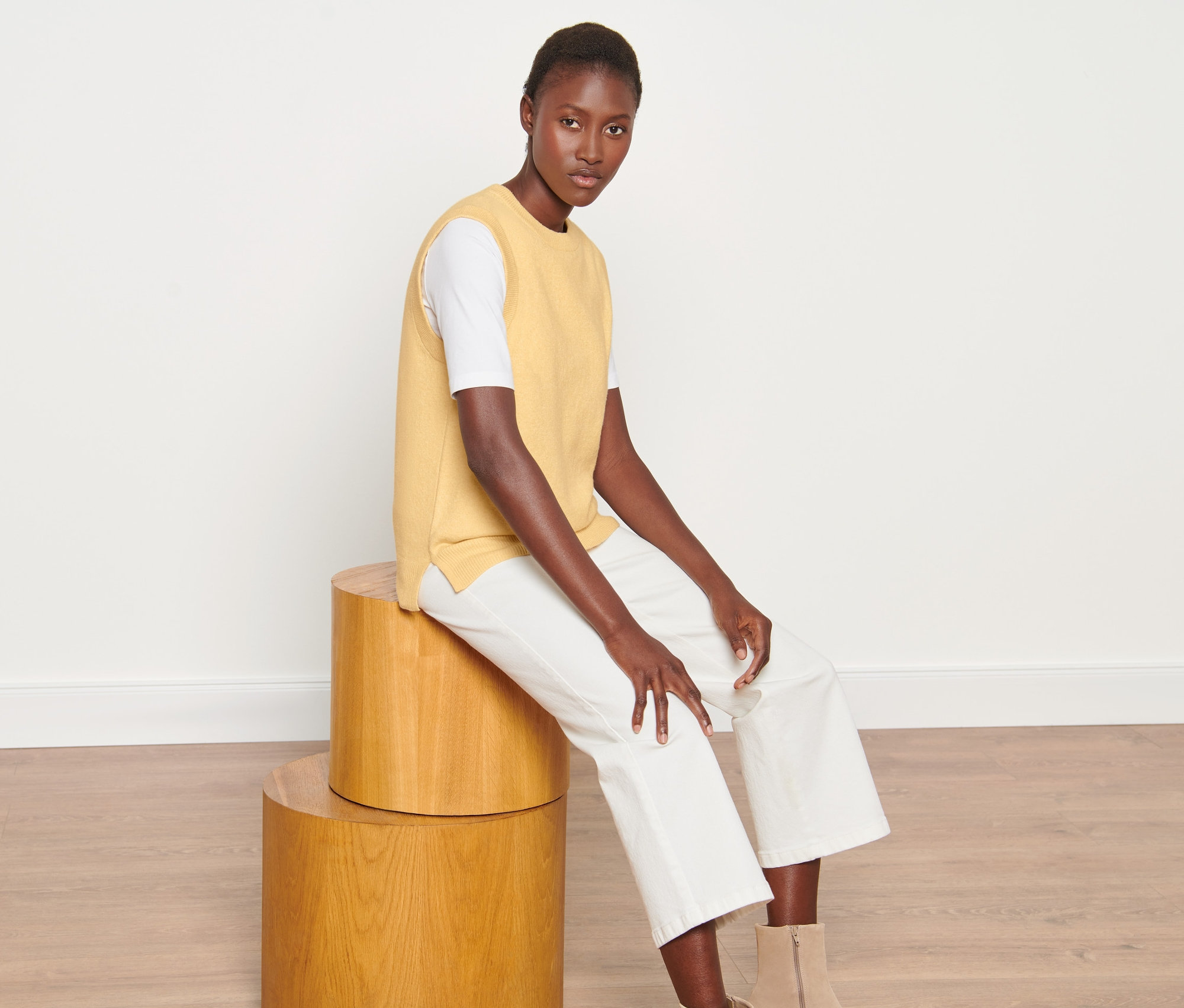 Frau sitzt auf Holzhockern und trägt einen Strickpullunder.