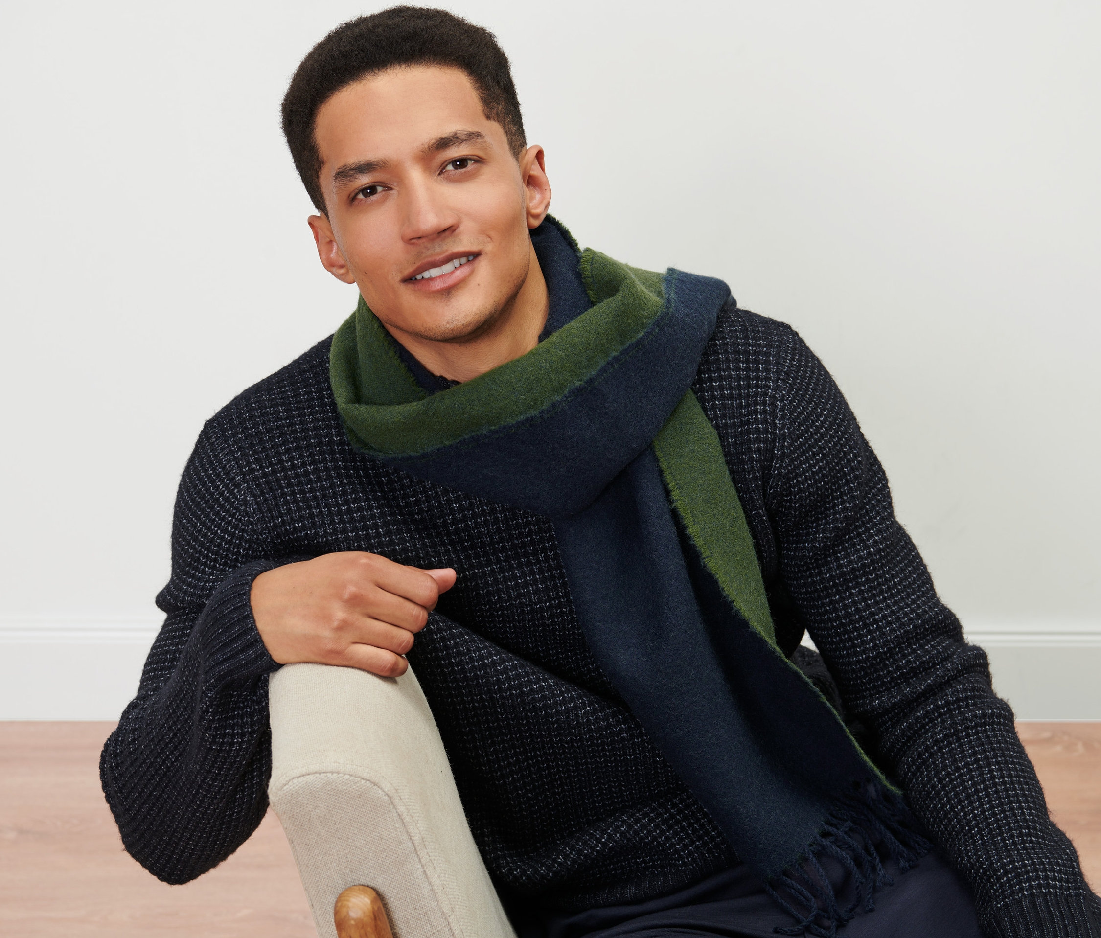 Mann sitzt auf einem Stuhl und trägt einen Webschal.