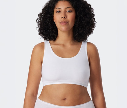 Eine Frau mit lockigem Haar trägt ein weißes SCHIESSER Bustier und einen weißen Slip.