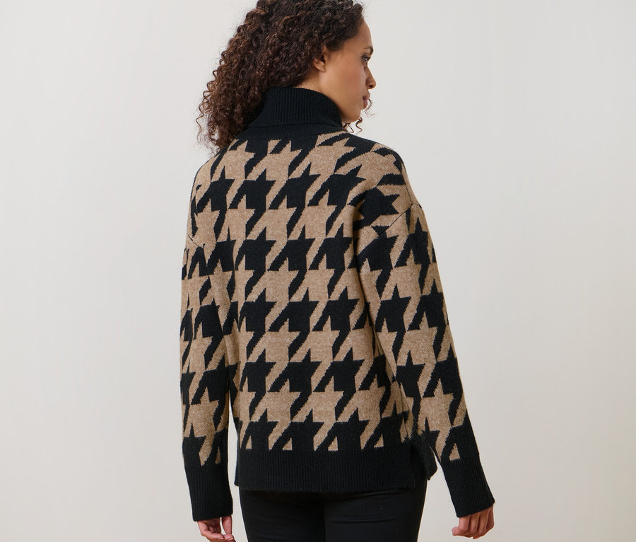 Frau mit lockigem Haar posiert mit dem Rücken zur Kamera und trägt einen Strickpullover mit Hahnentritt-Jacquard.