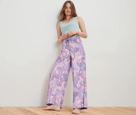 Frau posiert im Studio und trägt eine Web-Relaxhose mit Paisleymuster und ein hellgrünes Top.