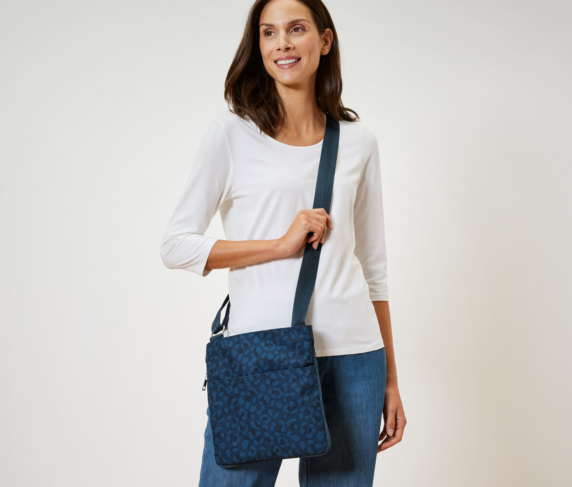 Frau mit dunklen Haaren und weißem Hemd posiert mit einer blauen Sicherheits-Umhängetasche.