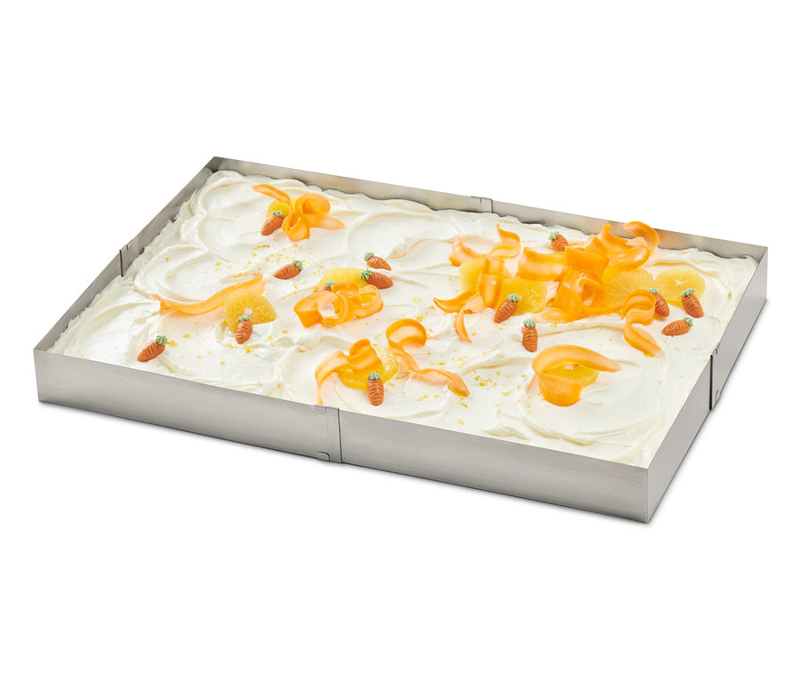Ein Kuchen, der mit Orangenschalen und Karotten in einem Edelstahl-Backrahmen dekoriert ist.