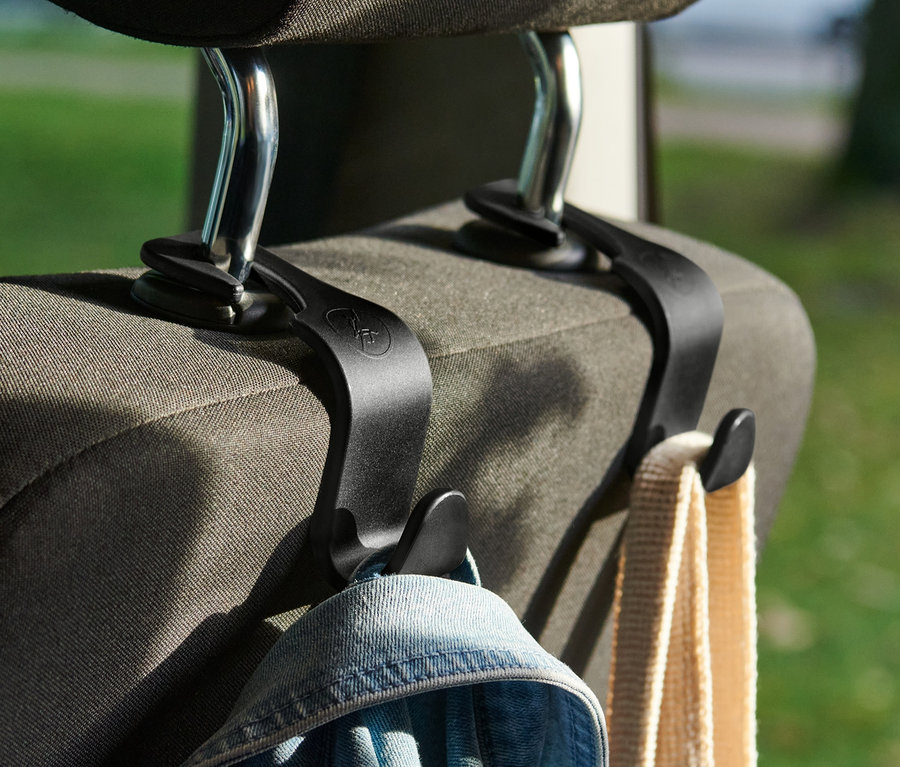 Zwei schwarze Kopfstützen-Haken sind an einem Autositz befestigt, an denen eine Jacke und eine Tasche hängen.
