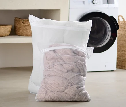 Zwei extragroße Wäschenetze stehen im Badezimmer vor einer Waschmaschine.