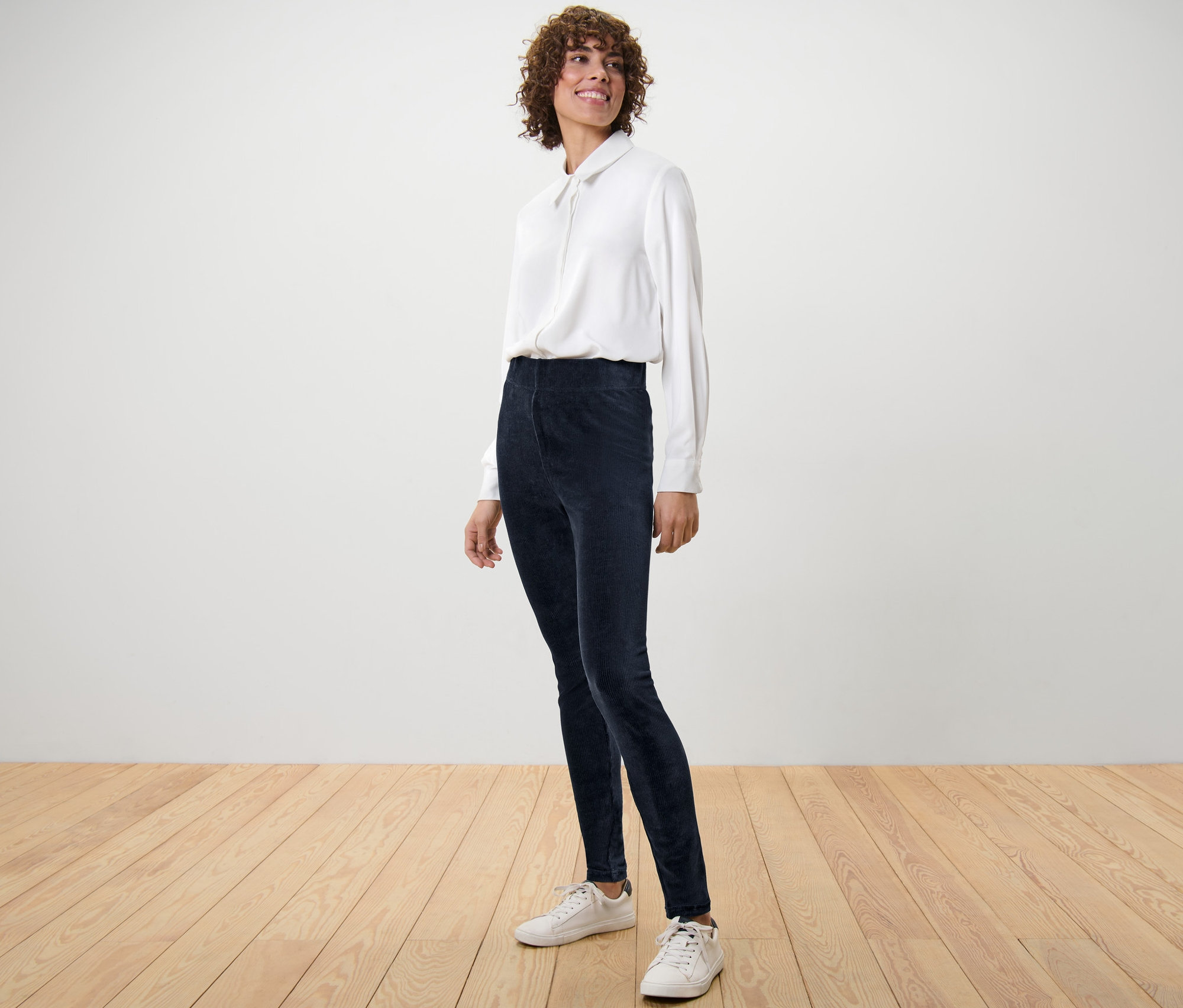 Frau posiert in Cord-Leggings und weißem Hemd.