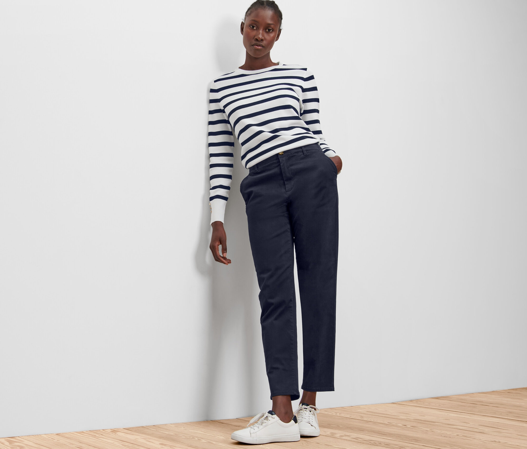 Eine Frau lehnt an einer Wand und trägt eine dunkelblaue Chino.