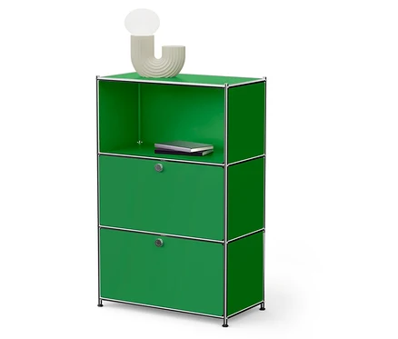 Grüner modularer Schrank mit zwei Türen und einem offenen Regal, auf dem ein Buch liegt. Oben steht eine Lampe.