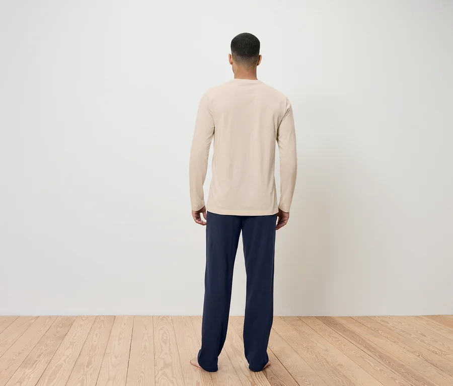 Ein Mann mit dem Rücken zur Kamera trägt ein beiges Langarmshirt und dunkelblaue Hosen.