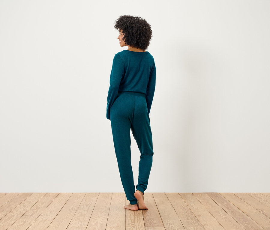 Frau mit Afro steht mit dem Rücken zum Betrachter und trägt ein smaragdgrünes Strickoberteil und eine Hose.
