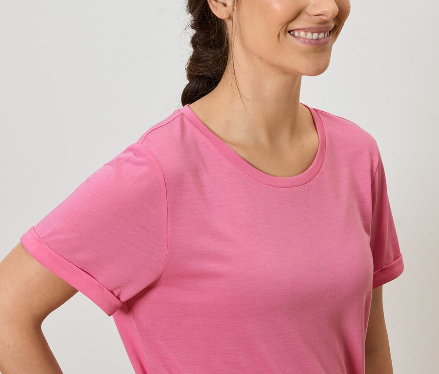 Frau mit braunen Haaren und einem Lächeln trägt ein rosa T-Shirt.
