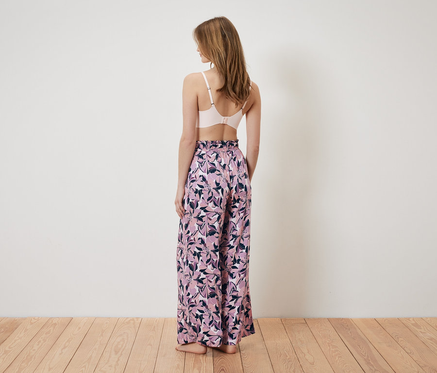 Frau von hinten trägt einen rosa BH und eine weite Hose mit Blumenmuster.