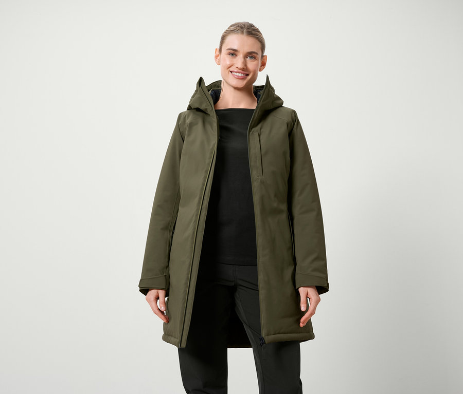 Frau posiert in olivgrüner Jacke mit Kapuze und schwarzer Kleidung.
