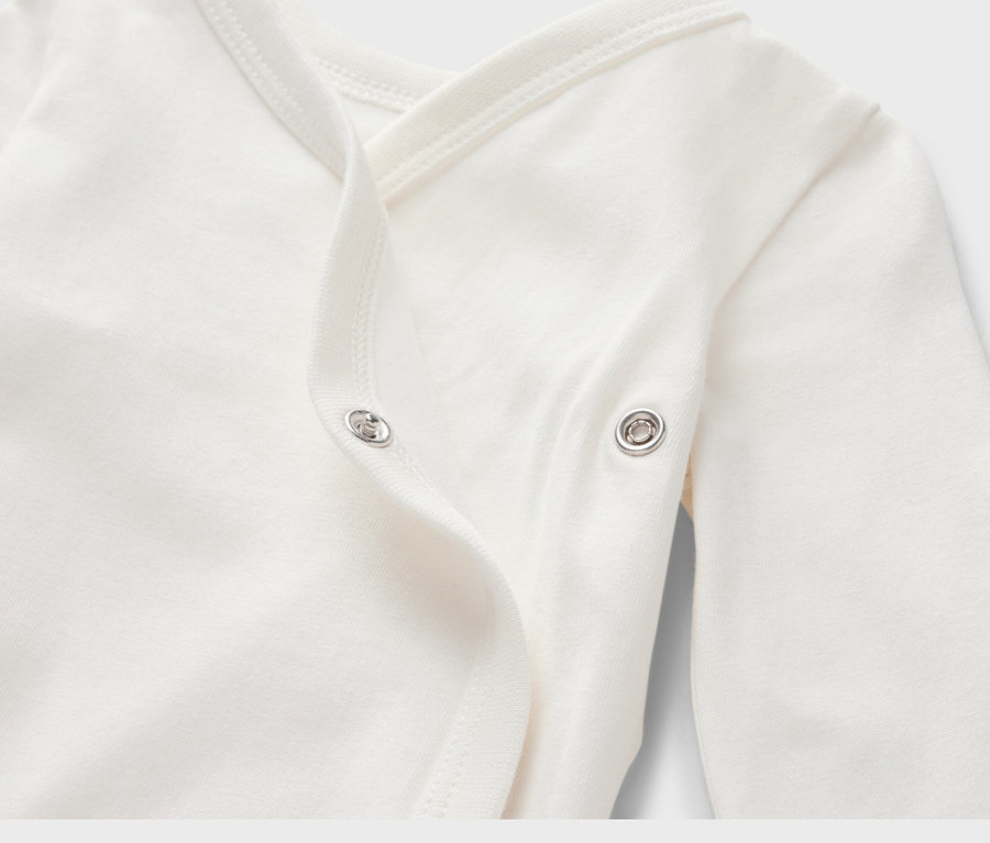 Detailansicht eines weißen Baby-Bodys mit Mitwachsfunktion, langen Ärmeln und Druckknopfverschluss.