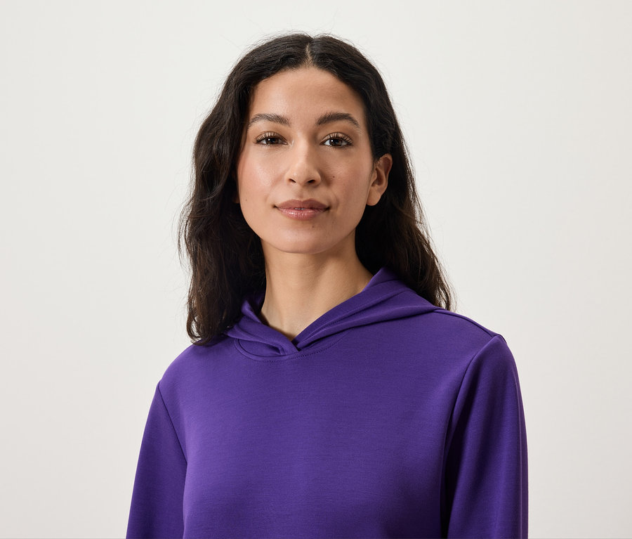 Porträt einer Frau mit dunklem Haar, die einen lila Kapuzenpullover trägt.