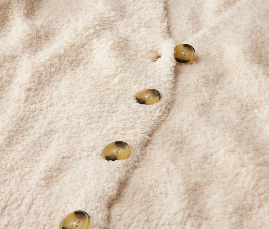 Detailaufnahme einer beige Strickjacke mit Knöpfen.