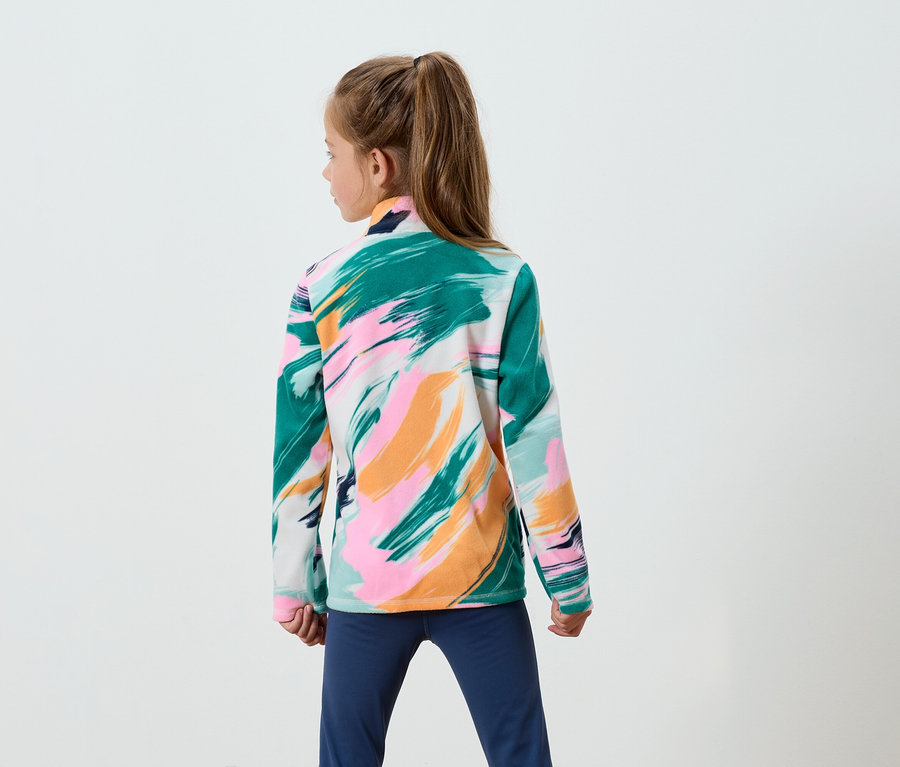 Ein Mädchen mit braunen Haaren im Pferdeschwanz steht mit dem Rücken zur Kamera und trägt eine Sweatshirtjacke mit Pinselstrichmuster in Grün, Rosa und Orange sowie eine blaue Hose.