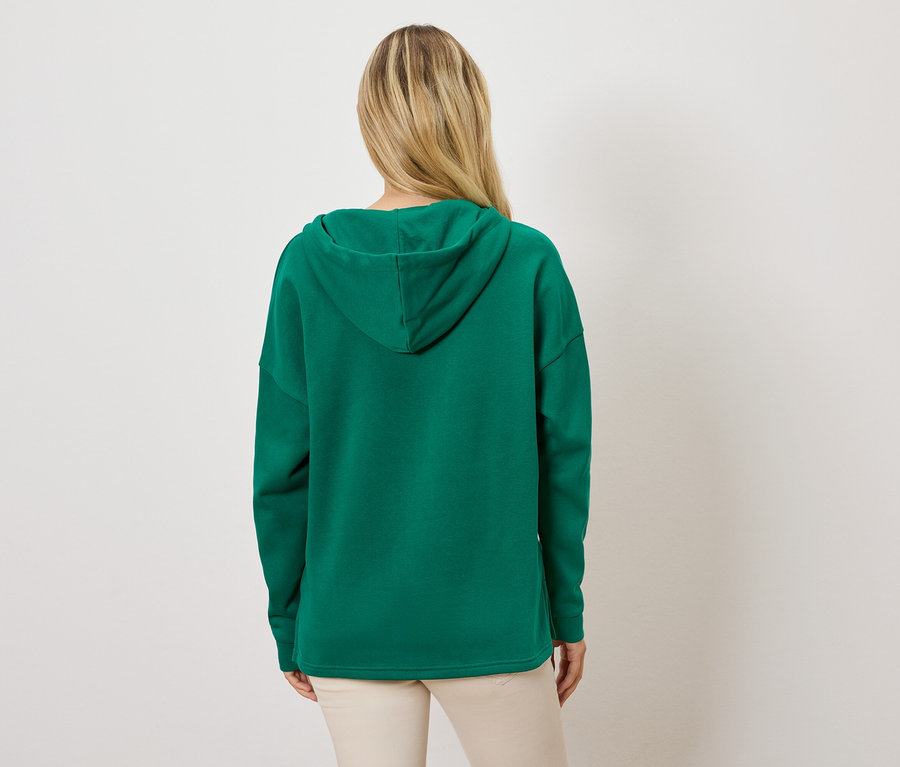 Frau mit dem Rücken zur Kamera trägt einen grünen Hoodie und helle Hosen.