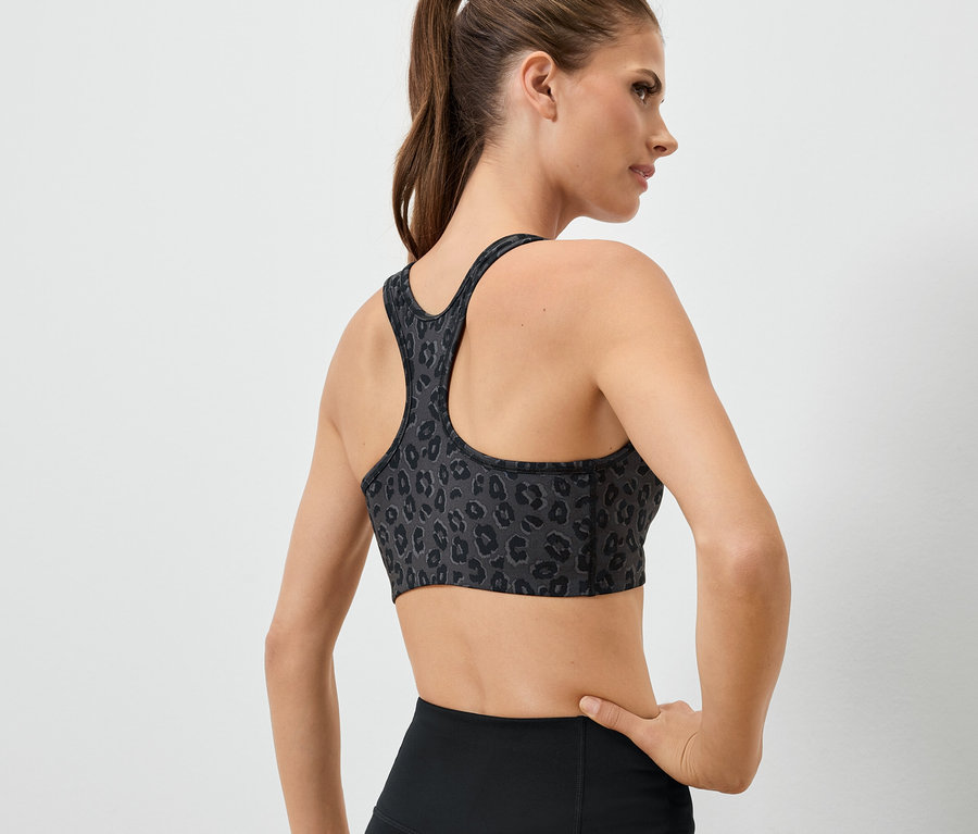 Frau mit dem Rücken zur Kamera, die einen Sport-BH mit Tiermuster und schwarze Leggings trägt.