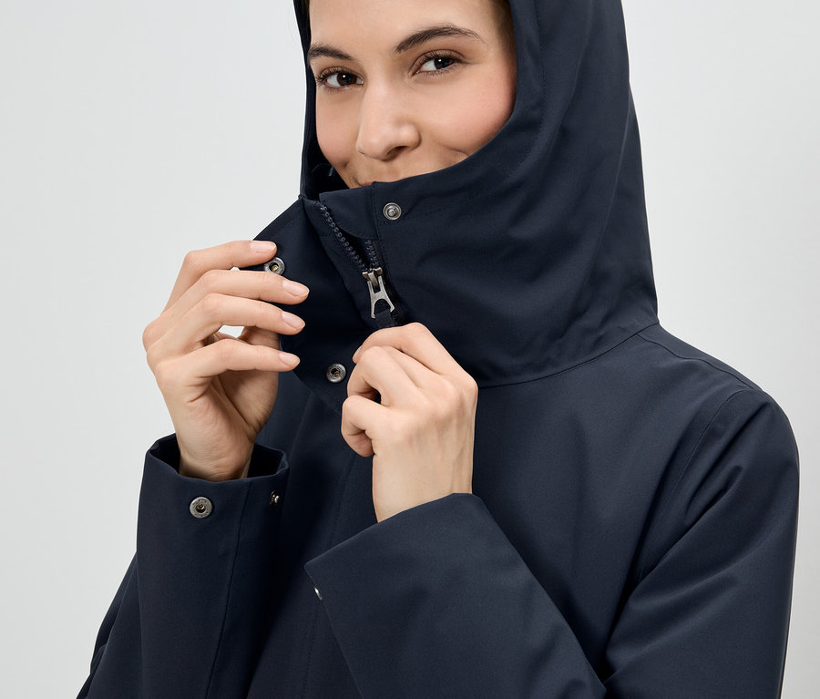 Frau schließt den Reißverschluss einer marineblauen Kapuzenjacke.