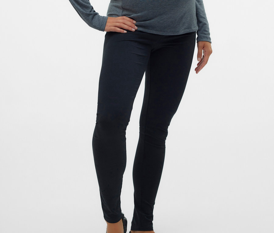 Schwangere Frau mit grauem Oberteil, schwarzen Leggings und Ballerinas.