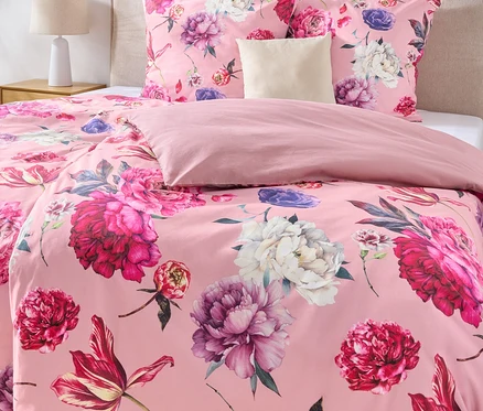 Nahaufnahme eines Bettes mit rosa Bettwäsche mit Blumenmuster, einem beigen Kopfteil und zwei gerahmten Bildern an der Wand.