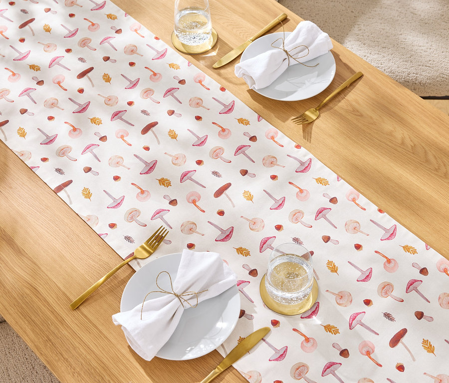 Tisch mit Pilzmuster-Tischläufer, goldenem Besteck, weißer Stoffserviette und einem Glas Wasser.
