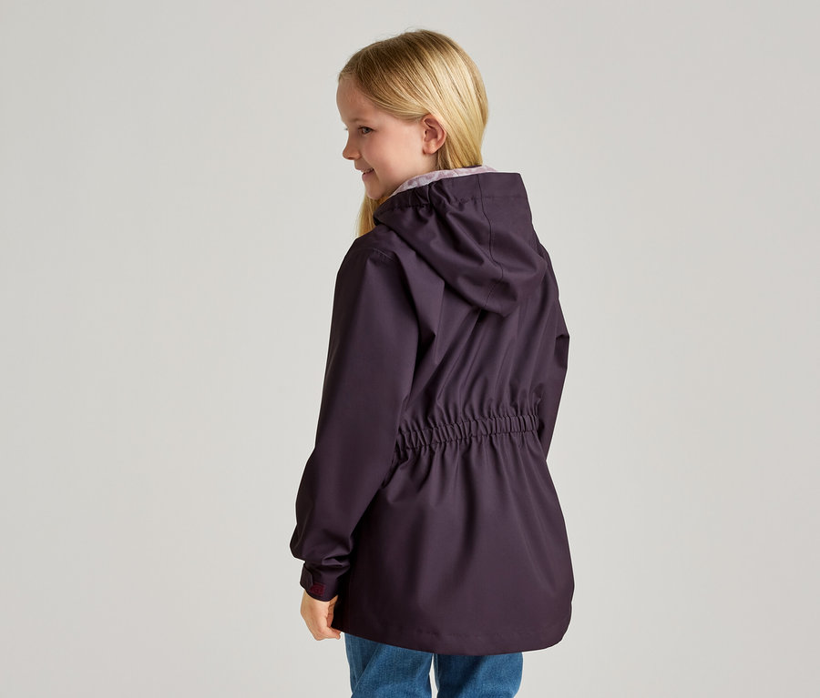 Eine junge, blonde Frau von hinten, die eine dunkelviolette Jacke mit Kapuze und Kordelzug an der Taille und blaue Jeans trägt.