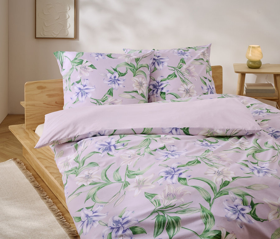 Bett mit lila Bettwäsche mit Blumenmuster und Holzrahmen.