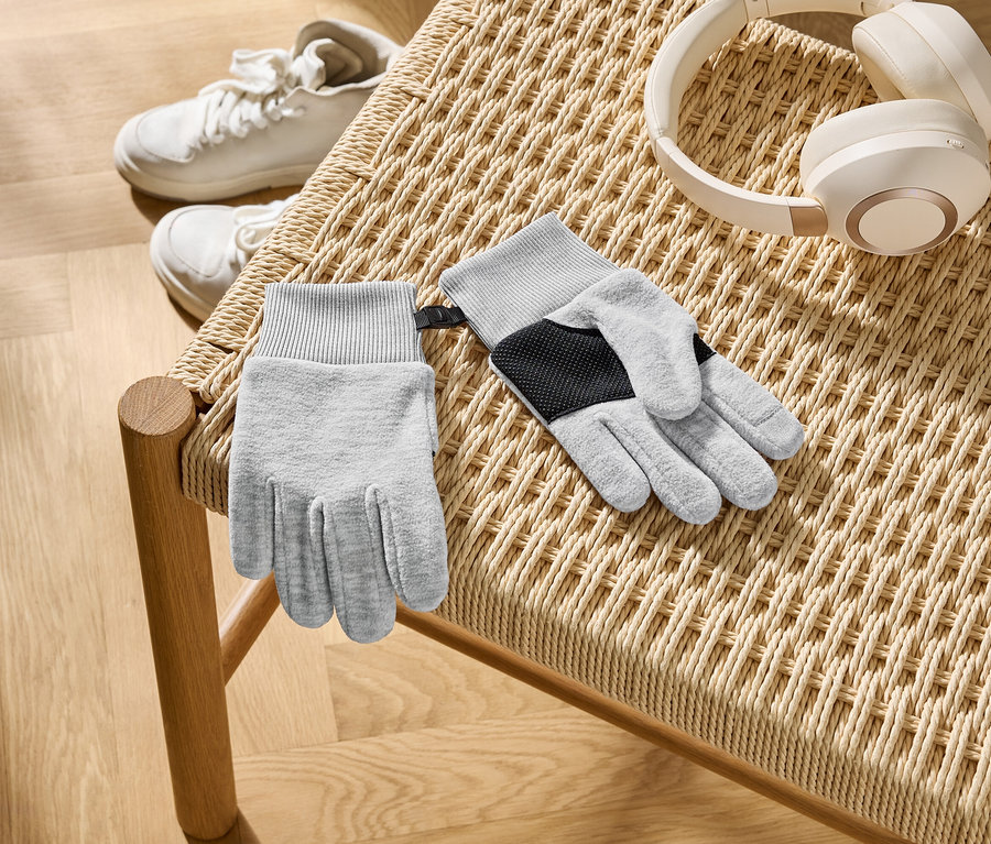 Auf einem geflochtenen Stuhl liegen graue Handschuhe, weiße Kopfhörer und weiße Turnschuhe.