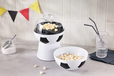 Ein Popcorn-Maker in Fußballoptik steht neben einer Schüssel Popcorn und einem Glas mit Strohhalmen.