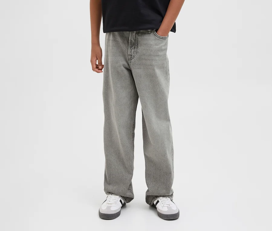 Eine Person trägt graue Jack&Jones JJOrginial Alex Jeans und weiße Sneaker. Eine Hand steckt in der Hosentasche.