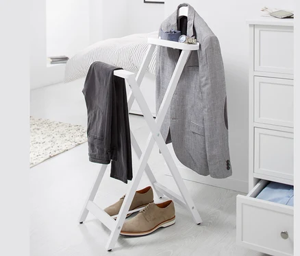 Auf einem weißen Hintergrund steht ein stummer Diener, an dem ein grauer Blazer und eine Hose hängen, darunter stehen braune Schuhe.