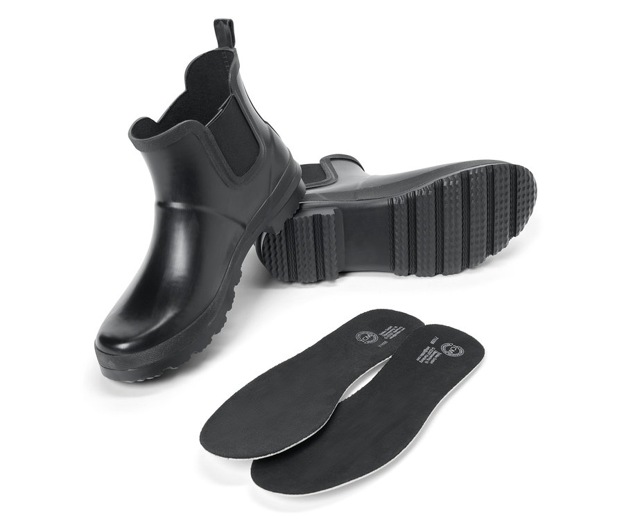 Zwei schwarze Gummistiefel und zwei schwarze Schuheinlagen auf einem weißen Hintergrund.