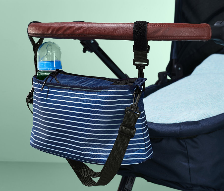 Ein blau-weiß gestreifter Organizer für Kinderwagen, der mit einer Flasche am Griff eines Kinderwagens befestigt ist.