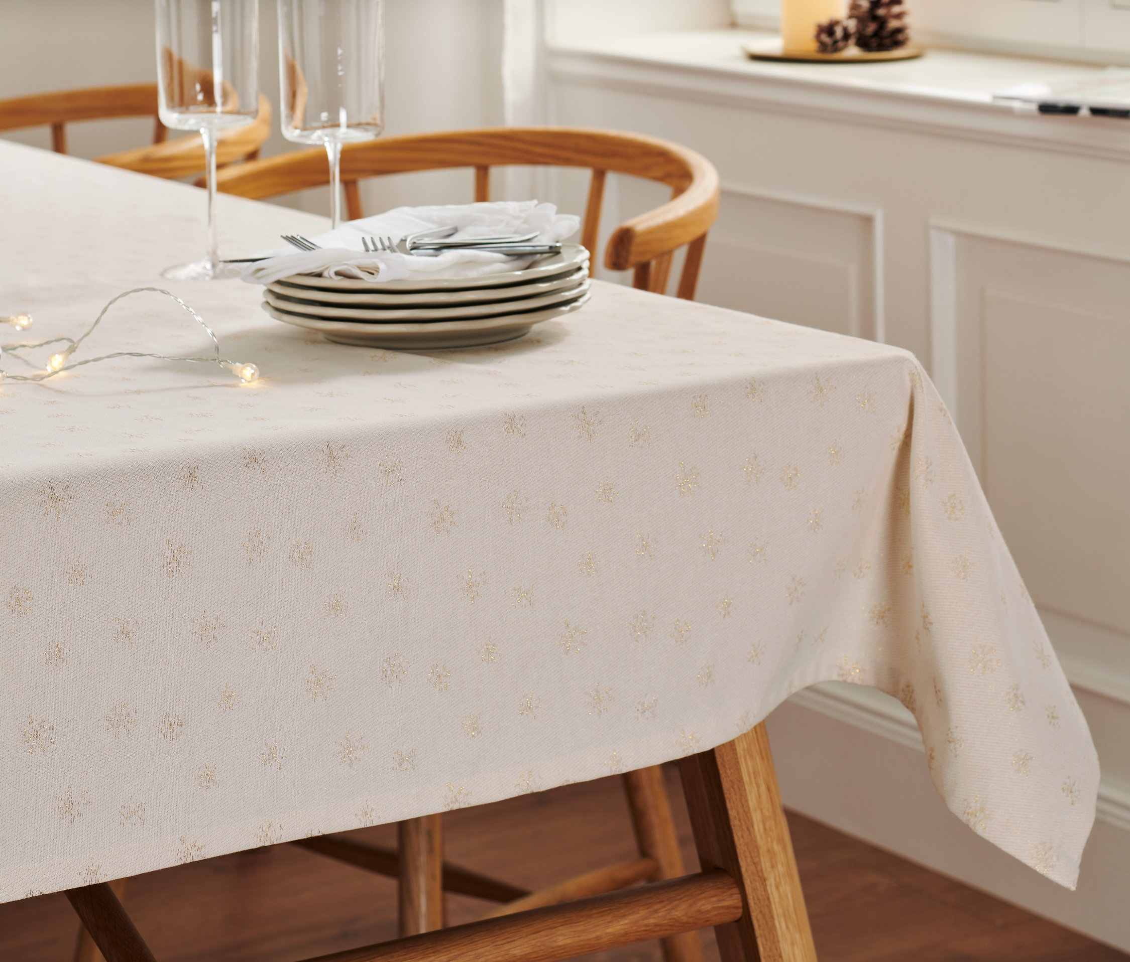 Auf einem Holztisch liegt eine Premium-Jacquard-Tischdecke mit Tellern, Besteck, Gläsern und einer Lichterkette.