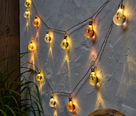 Eine LED-Lichterkette hängt an einer Wand, neben einer Pflanze.