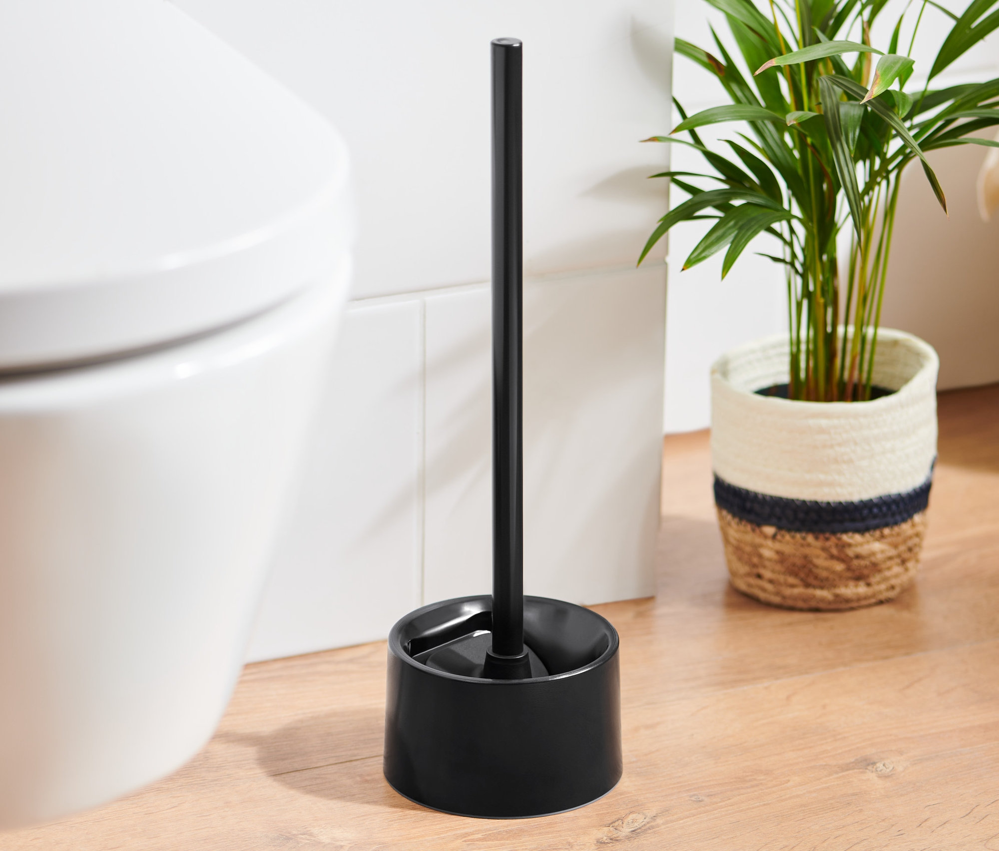 Eine schwarze Silikon-WC-Bürste steht neben einer weißen Toilette.