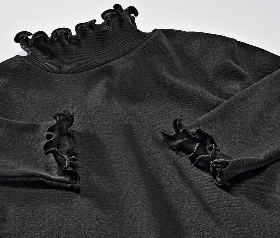 Detailaufnahme von einem Kinder-Langarmshirt mit Rüschen am Kragen und an den Handgelenken.