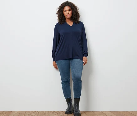 Eine Frau posiert in einem dunkelblauen Langarmshirt mit V-Ausschnitt, einer hellblauen Slim-Denim »Fit Emma« und Leder-Boots.