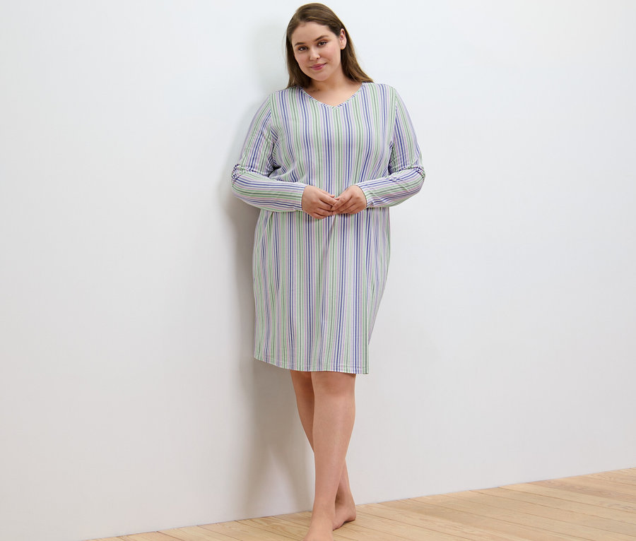 Frau im Nachthemd mit Streifen steht an der Wand.