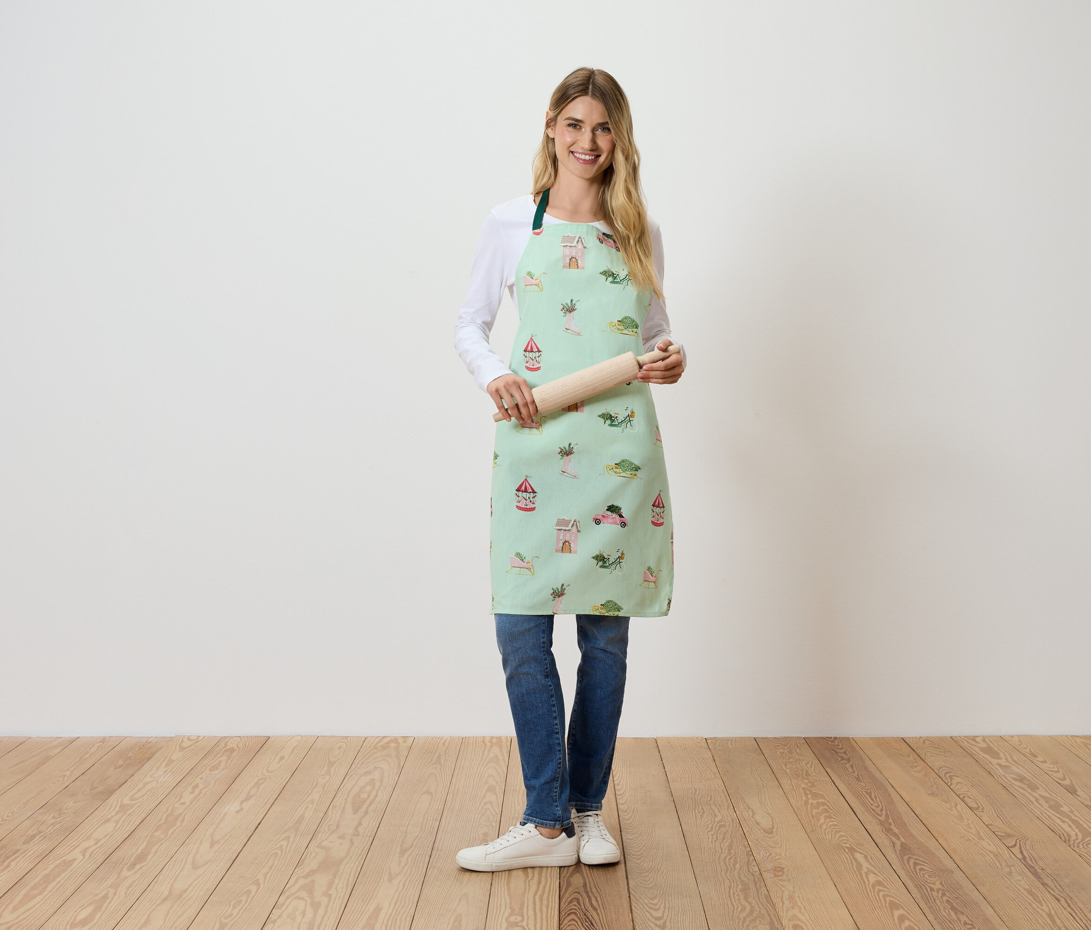 Eine Frau steht und hält einen Teigroller. Sie trägt eine hellgrüne Schürze mit Aufdruck.