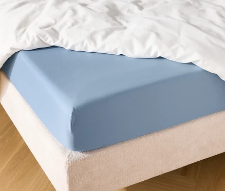 Hellblaues Spannbettlaken auf einem Bett mit weißer Bettdecke.