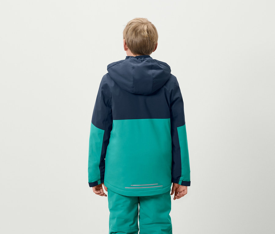 Junge steht mit dem Rücken zur Kamera, trägt eine blaugrüne Jacke und grüne Hosen.