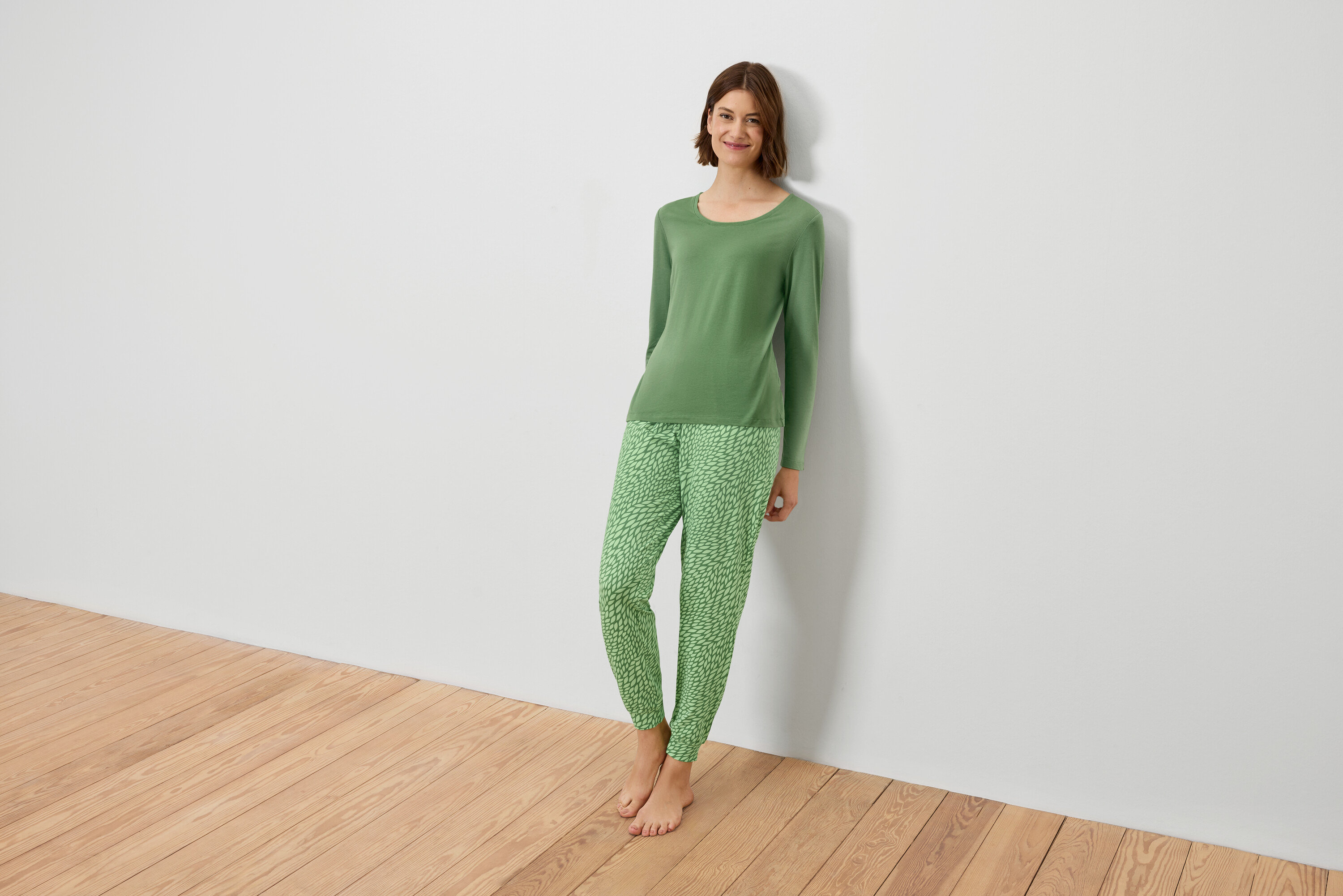 Frau im grünen Pyjama lehnt an einer weißen Wand.